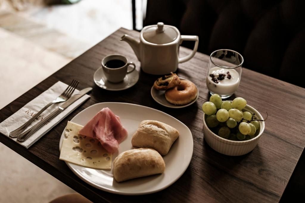 A breakfast setting with a plate of food, a teapot, a cup of coffee, a glass of milk with berries, and a bowl of grapes.