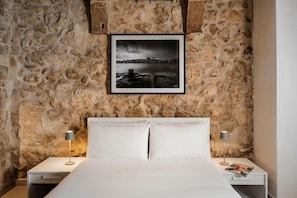 A bedroom with a stone wall, a framed photograph, a bed with white linens, and bedside lamps. - Casa Radiant (Rabat)
