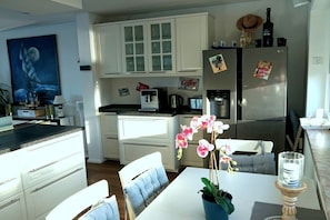 Eine moderne Küche mit weißen Schränken, einem Kühlschrank mit Magneten, einer Kaffeemaschine und einem Essbereich mit Tisch und Stühlen.