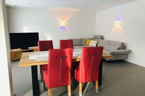Ein modernes Wohnzimmer mit einem Esstisch, roten Stühlen, einem grauen Sofa und zwei Wandleuchten.