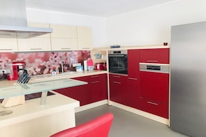 Eine moderne Küche mit roten Schränken, einem Edelstahlkühlschrank und einer Glas Arbeitsplatte.