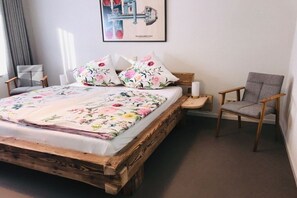 Ein Bett mit floralem Bettzeug, ein Holz-Kopfteil, ein Nachttisch mit Lampe und ein Sessel.