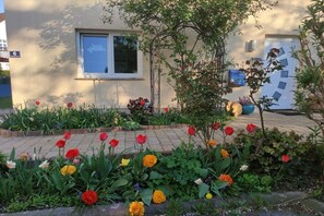 A building with a window and a door, surrounded by a garden with various flowers. - Holiday apartment with 1 bedroom (Markkleeberg)