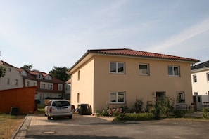 A residential building with a red-tiled roof, a car parked in the driveway, and a small garden with pink flowers. - Holiday apartment with 1 bedroom (Markkleeberg)
