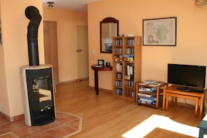 A living room with a wood-burning stove, a bookshelf, a television, and a map on the wall. - Holiday apartment with 1 bedroom (Markkleeberg)