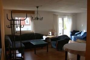 Uma sala de estar com sofá, poltronas, mesa de centro, lustre e janela com cortinas.