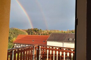 Ein Balkon mit Holzbalkon, der auf einen Wohnbereich mit Häusern und einer Hügelkulisse blickt.