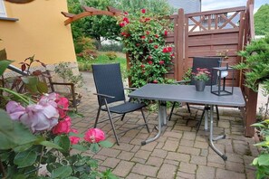 An outdoor patio with a table and chairs, surrounded by potted plants and a wooden fence. - Holiday apartment with 1 bedroom (Porschdorf)