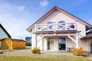 Une maison à deux étages avec un balcon, un abri de jardin en bois et une allée pavée.