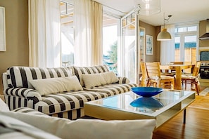 A living room with a striped sofa, a glass coffee table, and a dining area with wooden chairs and a table. - Holiday apartment with 3 bedrooms (Zinnowitz)