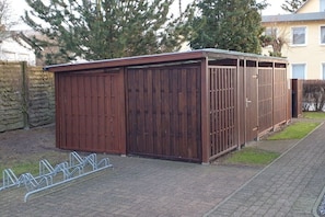 A wooden shed with a metal roof, a metal fence, and a paved walkway. - Holiday apartment with 1 bedroom (Koserow)