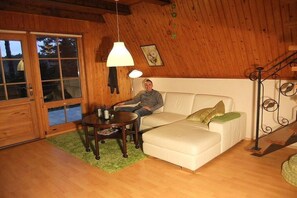 A cozy living room with a wooden ceiling, a white sofa, a small round table, and a floor lamp. - Finnish-style cabin in a quiet location by the lake (Garden)