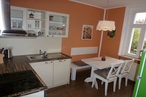 A kitchen with white cabinets, a wooden countertop, a stove, and a dining area with a table and chairs. - Holiday apartment with 2 bedrooms (Dresden)