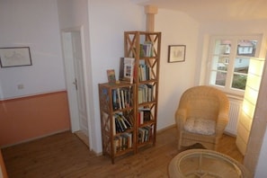 A room with a wooden bookshelf, a wicker chair, and a window with a view of houses. - Holiday apartment with 2 bedrooms (Dresden)