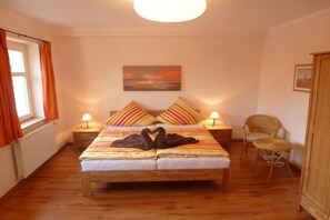 Une chambre à coucher avec un lit double, deux tables de chevet avec des lampes, une chaise, un tableau au mur et une fenêtre avec des rideaux.