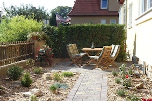 A patio with a table and chairs, surrounded by a garden with various plants and a wooden fence. - Holiday apartment with 2 bedrooms (Dresden)