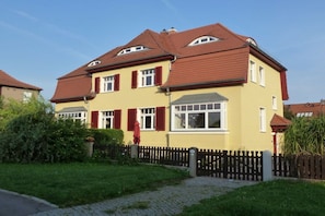 A two-story house with a red-tiled roof, a yellow facade, and a black picket fence. - Holiday apartment with 2 bedrooms (Dresden)