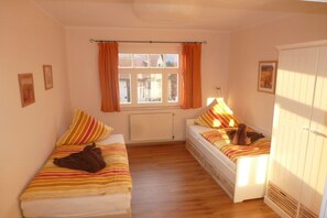 Een slaapkamer met twee enkele bedden, een raam met gordijnen, een radiator en een kledingkast.
