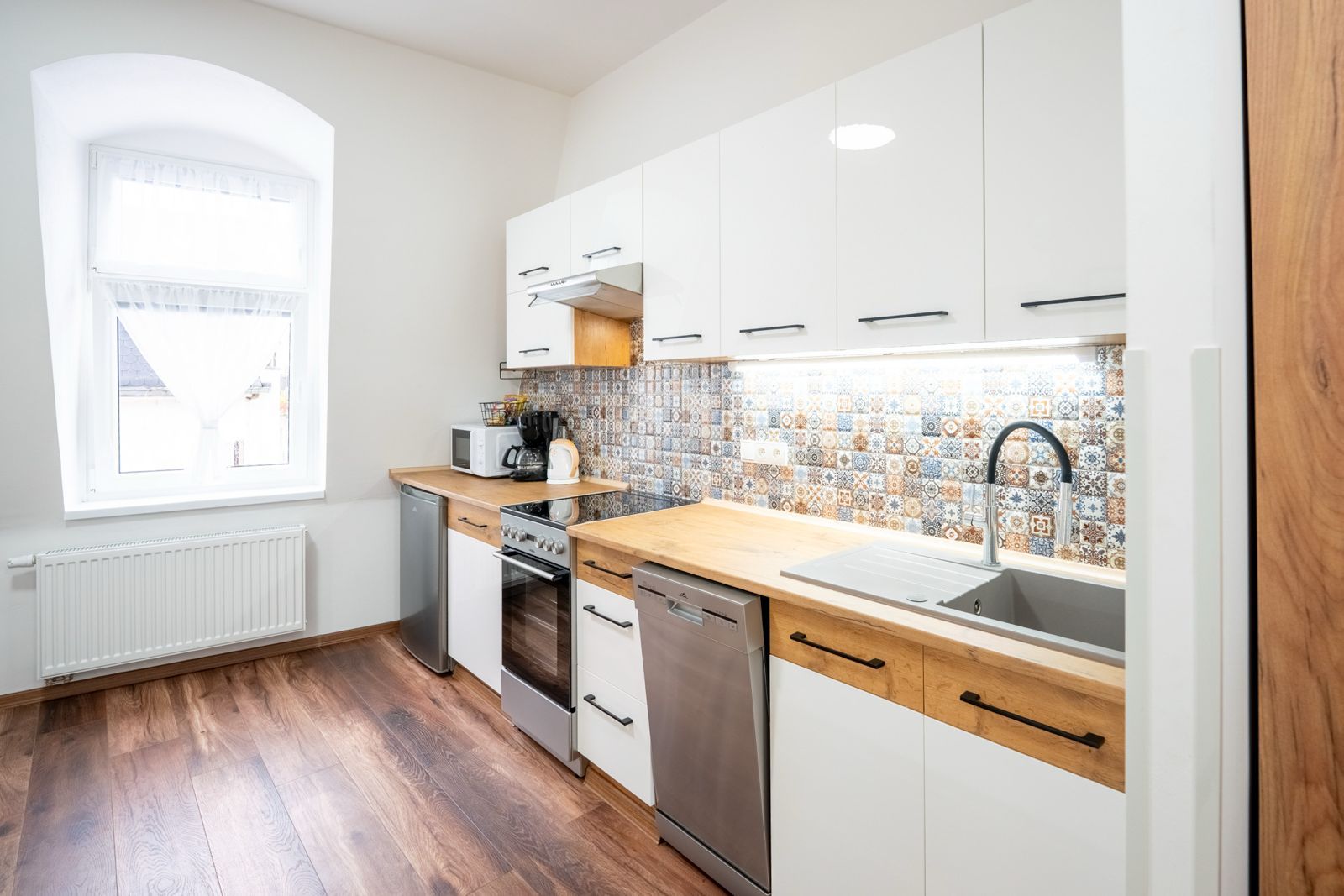 Eine moderne Küche mit weißen Schränken, einer Holzauskleidung, einem eingebauten Backofen, einem Geschirrspüler und einem Fenster mit Blick auf ein Gebäude.