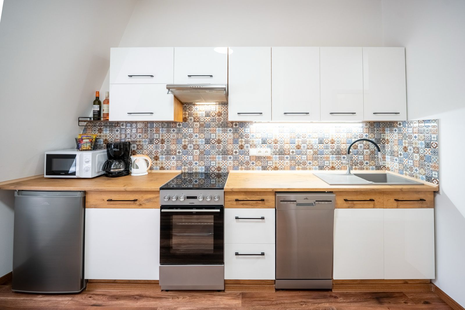 Cocina compacta con gabinetes blancos, microondas, estufa, lavavajillas y un lavamanos.