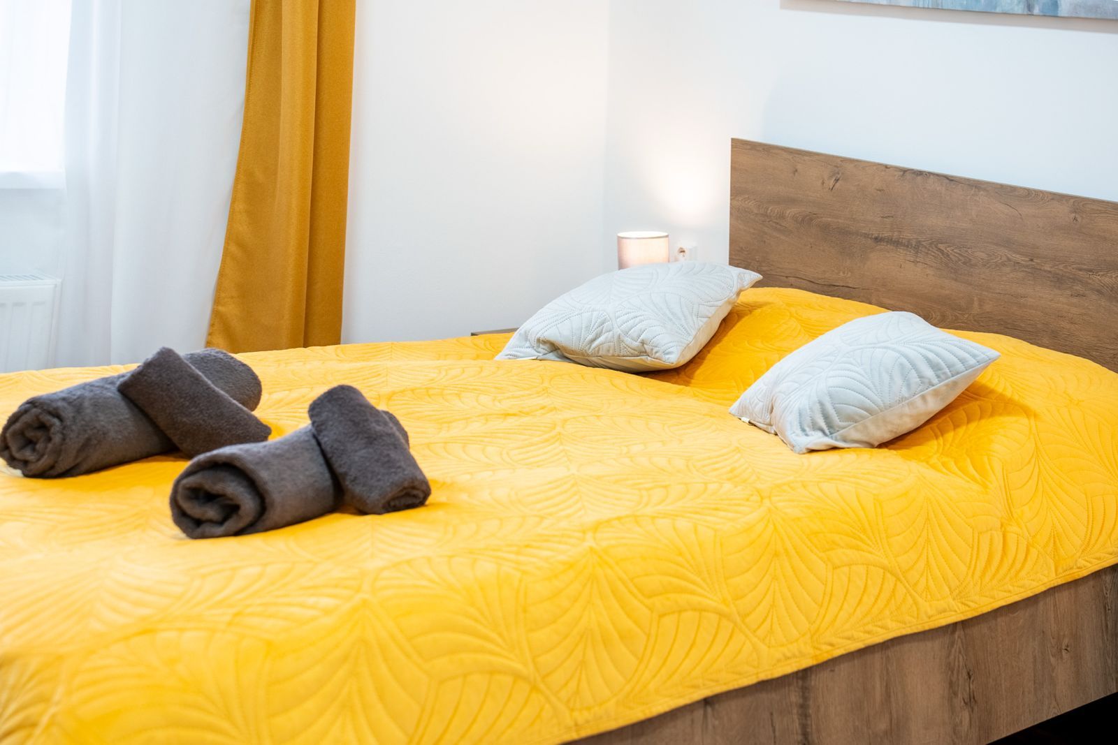 A bed with a yellow bedspread, two pillows, and rolled towels.