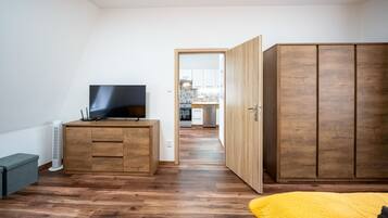 Une chambre avec une armoire en bois, un téléviseur posé sur une commode en bois et une couvre-lit jaune.