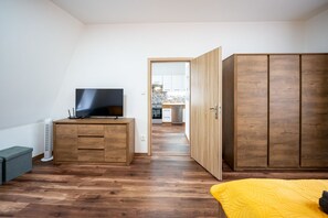 Une chambre avec une armoire en bois, un téléviseur posé sur une commode en bois et une couvre-lit jaune.