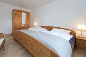 Ein Schlafzimmer mit einem hölzernen Bett, einem Kleiderschrank, zwei Nachttischlampen und einem Korbstuhl.
