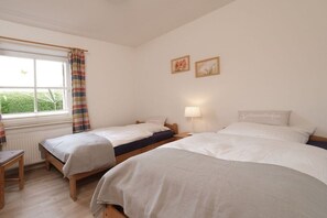 Quarto com duas camas, uma janela com cortinas, mesa de cabeceira e abajur.