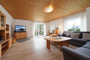 Uma sala de estar com teto de madeira, um sofá, uma televisão e uma mesa de jantar.