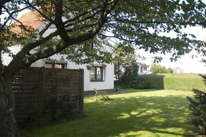Une maison blanche avec une clôture en bois, une pelouse bien entretenue et un grand arbre qui offre de l’ombre.