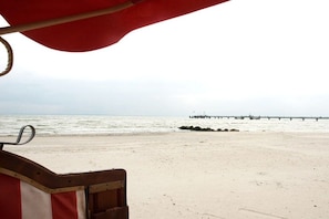 Une plage avec une jetée visible au loin et un parasol rouge au premier plan.