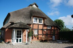 A traditional thatched-roof building with a brick facade, a wooden bench, and a gravel ground. - Holiday apartment in Nieby with swimming pool (Nieby)