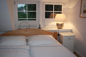 Ein Schlafzimmer mit einem Bett, zwei Fenstern, einer Nachttischlampe und einem Nachttisch.