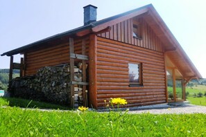 Eine Blockhütte mit Steinmauer, einer Holzleiter und einer Glashaus.