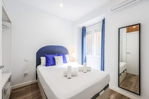 Een hotelkamer met een bed, nachtkastje, lamp, spiegel en een raam met gordijnen.