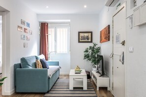 A compact living space with a sofa, a small table, a television, and a door. - Modern Apartment in Madrid Near the Royal Palace (Madrid)