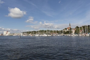 A waterfront cityscape with a prominent church spire, a marina with sailboats, and a row of buildings along the shore. - Holiday apartment with 2 bedrooms (Flensburg)