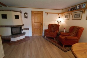A living room with a fireplace, two armchairs, a wooden coffee table, and a bookshelf with books and framed pictures. - Bungalow with 2 bedrooms (Reinhardtsdorf-Schöna)
