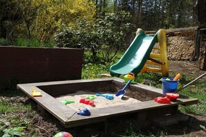 A sandbox with a slide and toys, surrounded by greenery. - Bungalow with 2 bedrooms (Reinhardtsdorf-Schöna)