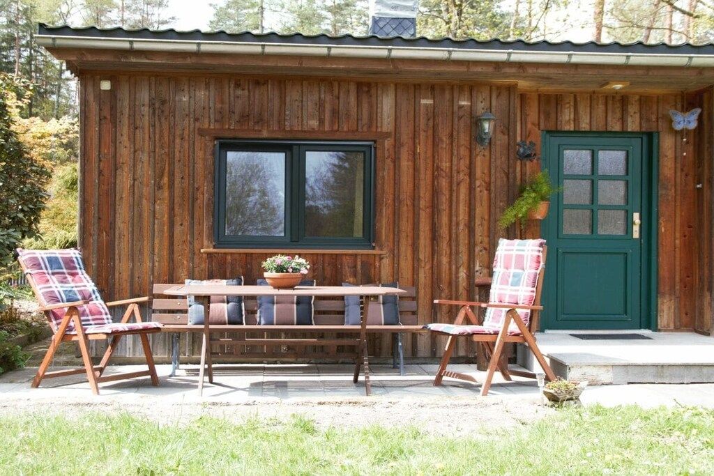 A wooden cabin with a green door, a window, and a table with chairs.