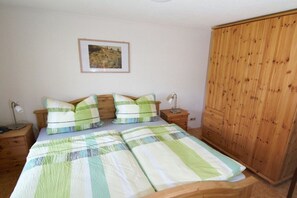 A bedroom with a bed, two bedside tables, a wooden wardrobe, and a framed picture on the wall. - Bungalow with 2 bedrooms (Reinhardtsdorf-Schöna)