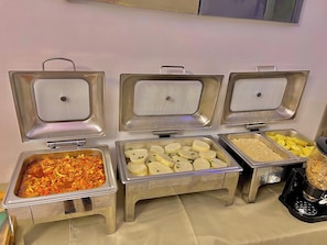 Buffet amb diversos plats, incloent un plat amb verdures, un safata de cubs blancs i un recipient amb fruita groga.