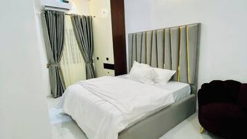 Een moderne slaapkamer met een groot bed, een donkergroene fauteuil en een wandairconditioning.