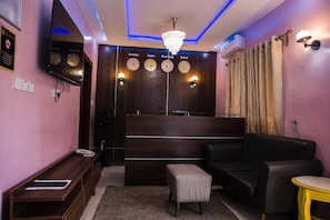 Un salon moderne avec un téléviseur à écran plat, un lustre, un canapé, un pouf et une petite table ronde.