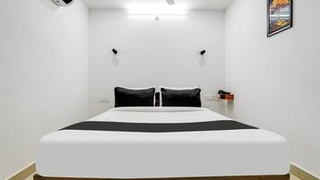 Quarto com cama, ventoinha no teto, ar condicionado na parede, mesa de cabeceira com telefone e quadro na parede.