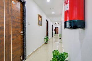 A hotel corridor with wooden doors, a fire extinguisher, potted plants, and a framed artwork on the wall. - Collection O De Alphabet Hotel (Hyderabad)