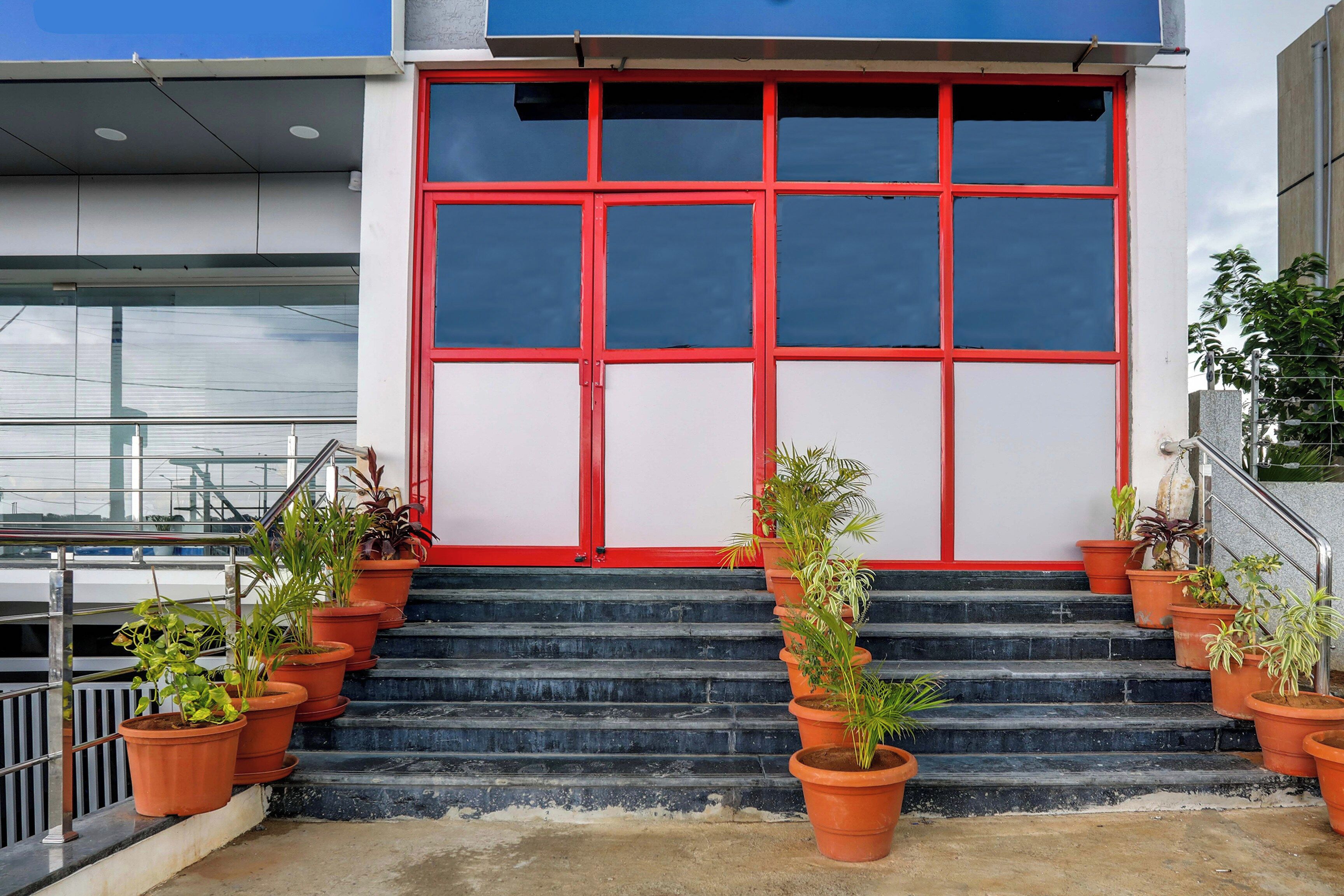 Fachada de un edificio con puerta roja, varias macetas con plantas y una escalera que conduce a la entrada.