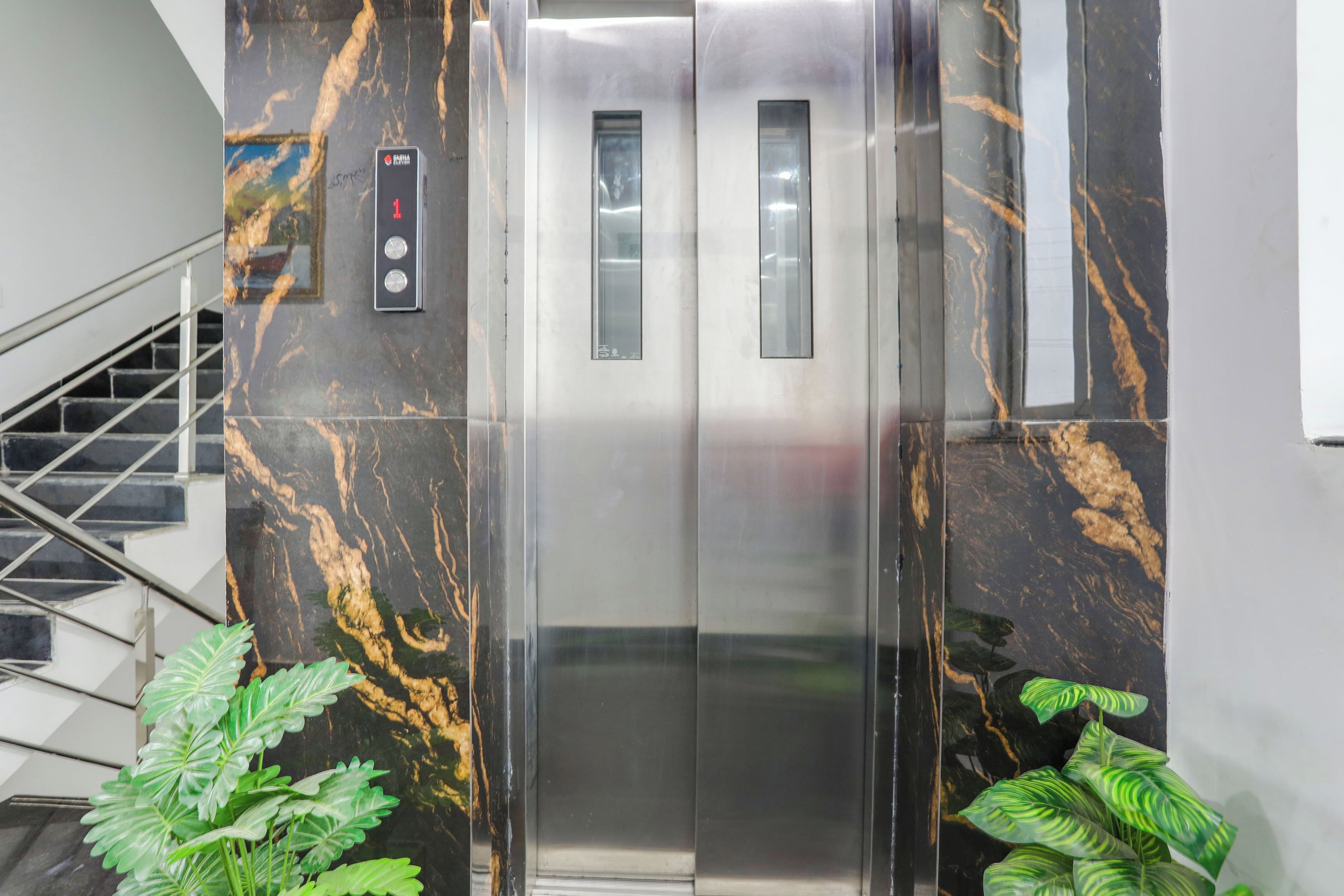 Un ascensor con pantalla digital, paredes metálicas y una escalera a la izquierda.