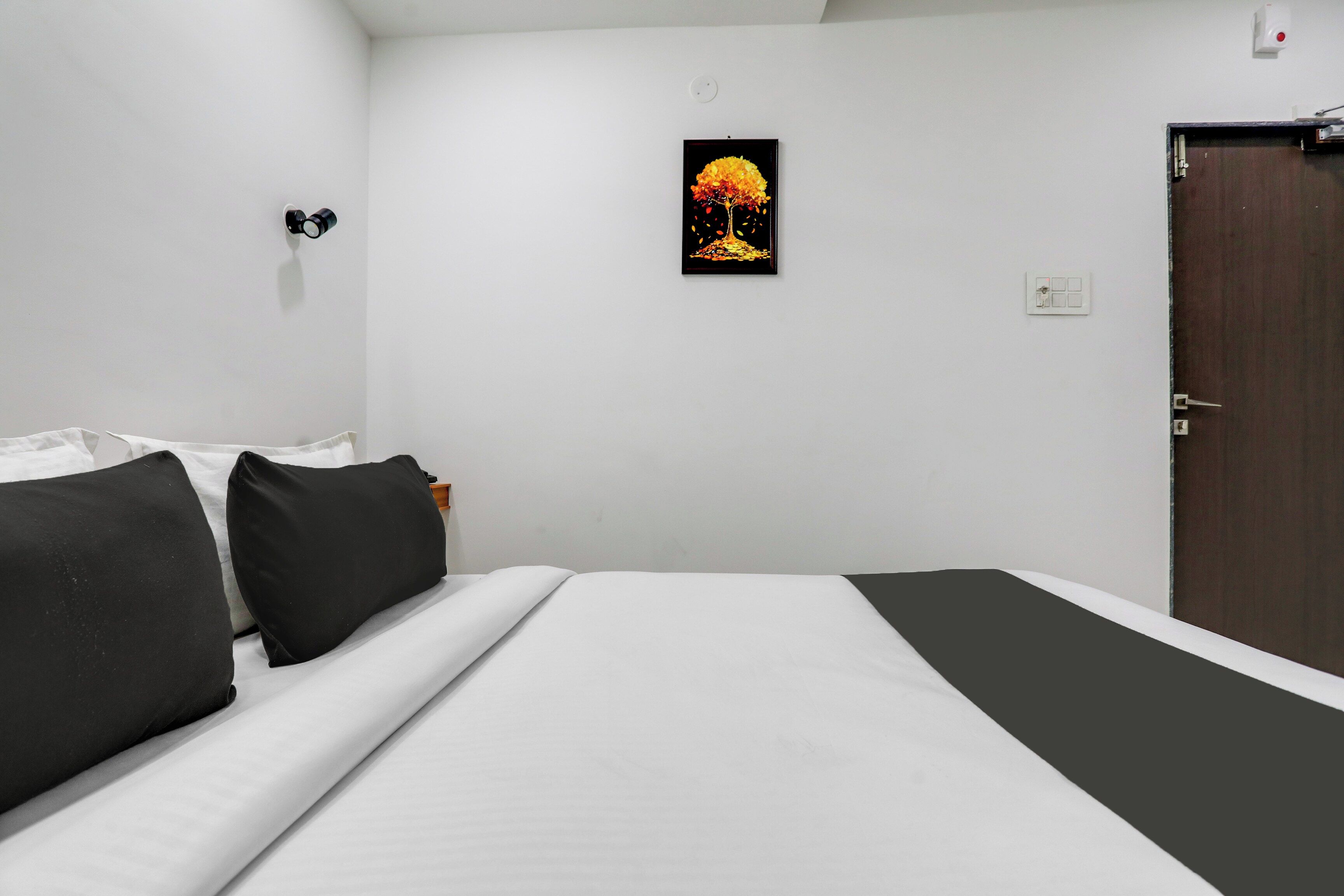 Ein Hotelzimmer mit einem Bett, einer Tür, einem an der Wand befestigten Lichtschalter und einem gerahmten Bild.